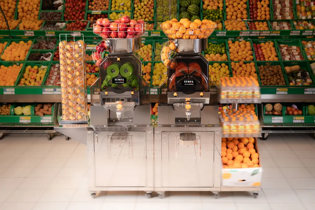 Presse-agrumes professionnels SEMPA installés en rayon fruits avec oranges et jus frais